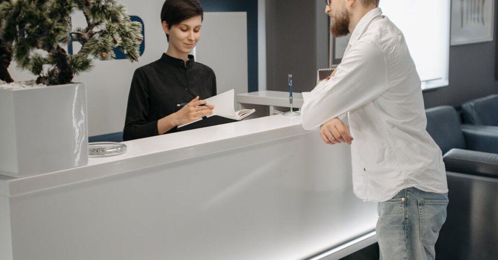 A man and woman at a sleek office reception desk, discussing paperwork in a professional setting.